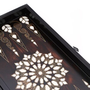 Peut inclure: Un plateau de jeu de backgammon en bois avec un cadre noir et des motifs complexes en nacre incrust&eacute;s. Le plateau pr&eacute;sente un motif circulaire central et des points de backgammon traditionnels.