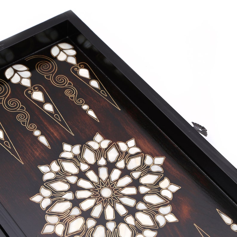 Peut inclure: Un plateau de jeu de backgammon en bois avec un cadre noir et des motifs complexes en nacre incrust&eacute;s. Le plateau pr&eacute;sente un motif circulaire central et des points de backgammon traditionnels.
