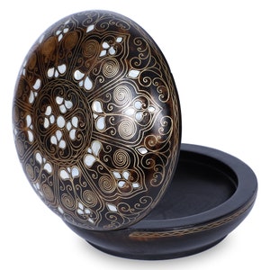May include: A round wooden box with a lid decorated with a black and gold floral pattern and white mother of pearl accents. The box is open and the inside is black.