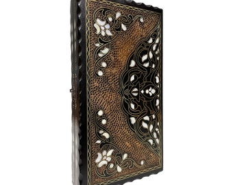 Puede incluir: Una caja de juego de madera con intrincados diseños de nácar negro y dorado incrustados. La caja tiene un fondo marrón y un borde ondulado.