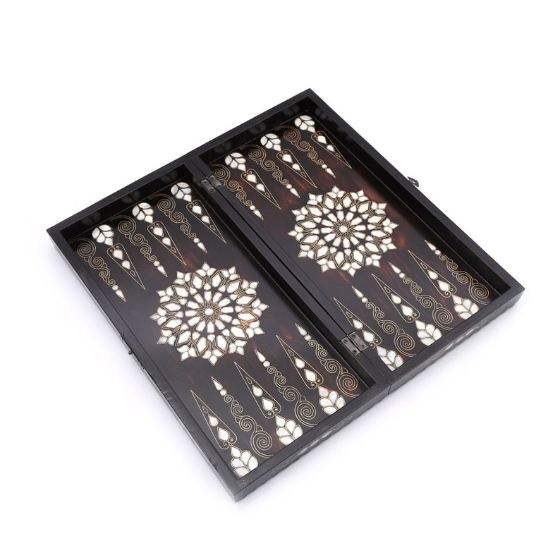Peut inclure: Un jeu de backgammon en bois noir avec des motifs complexes en incrustation blanche et dor&eacute;e. Le plateau est ouvert et pr&ecirc;t &agrave; jouer.