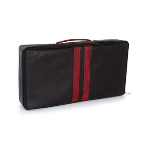 Peut inclure: Valise de voyage noire avec une bande rouge au centre. La valise a une fermeture &eacute;clair et une poign&eacute;e.