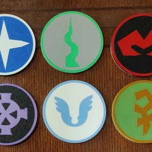 以下が含まれることがあります： 異なるデザインの丸いコースター6枚。コースターは質感のある素材でできており、青、緑、赤、白、黒、金など、さまざまな色があります。