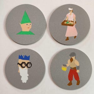Op de afbeelding: Vier ronde grijze onderzetters met verschillende cartoonfiguren erop geschilderd. De figuren omvatten een groene elf, een vrouw in een roze jurk die een dienblad draagt, een man met een blauwe kroon en bril, en een man met een rode baard en rode broek die een gele emmer vasthoudt.