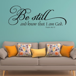 May include: A living room with a light blue wall and a beige sofa with orange and floral patterned cushions. The wall has a black vinyl decal with the text "Be still and know that I am God. Psalm 46:10."