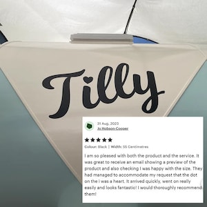 May include: Black vinyl sticker with the name "Tilly" in a cursive font with a heart in the "i". The sticker is on a light blue and white surface. The sticker is 55 centimeters wide.