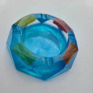 May include: A blue, octagonal ashtray with a geometric design. The ashtray has four small, colorful, gummy bear-shaped accents.