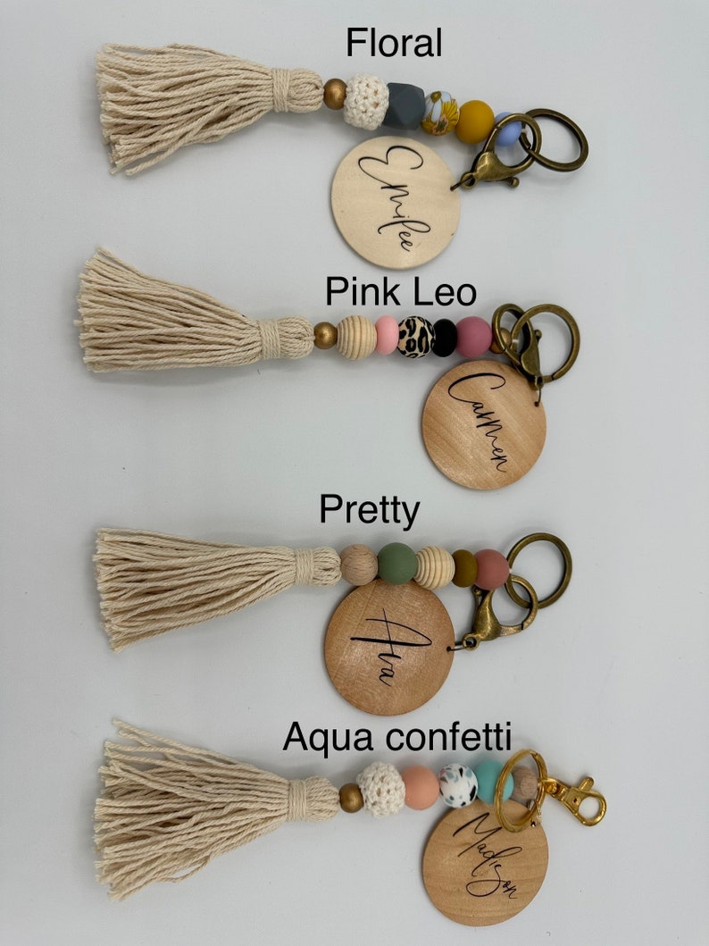 K&ouml;nnte beinhalten: Vier Holzschl&uuml;sselanh&auml;nger mit verschiedenen bunten Perlen und Quasten. Die Schl&uuml;sselanh&auml;nger sind mit "Emilee", "Camren", "Ava" und "Madison" beschriftet.