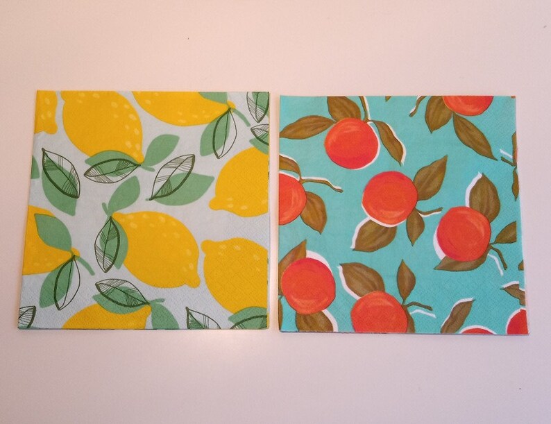 May include: Two paper napkins with a summer fruit theme. One napkin has a yellow lemon pattern on a light blue background. The other napkin has a red orange pattern on a turquoise background.