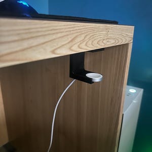 Puede incluir: Un escritorio de madera con un soporte de carga para Apple Watch de metal negro adjunto. El soporte contiene un Apple Watch plateado y un cable de carga blanco. El escritorio tiene una alfombrilla de ratón negra y un ratón negro.