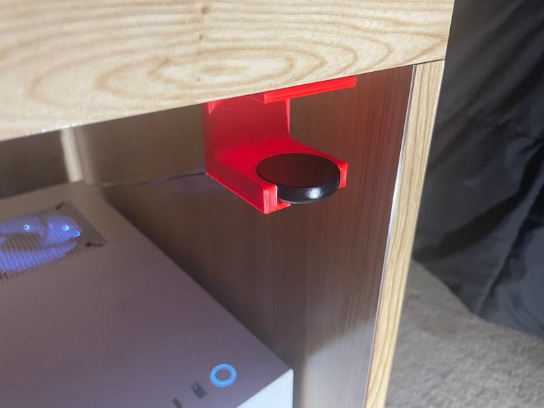 May include: A red 3D printed hook mounted under a wooden shelf with a black round object hanging from it.