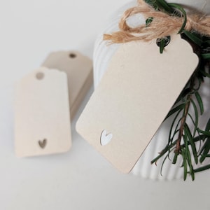 Könnte beinhalten: Ein Stapel brauner Geschenkanhänger mit einem weißen Herz-Ausschnitt. Die Anhänger sind mit Schnur und einem Zweig Grün gebunden.