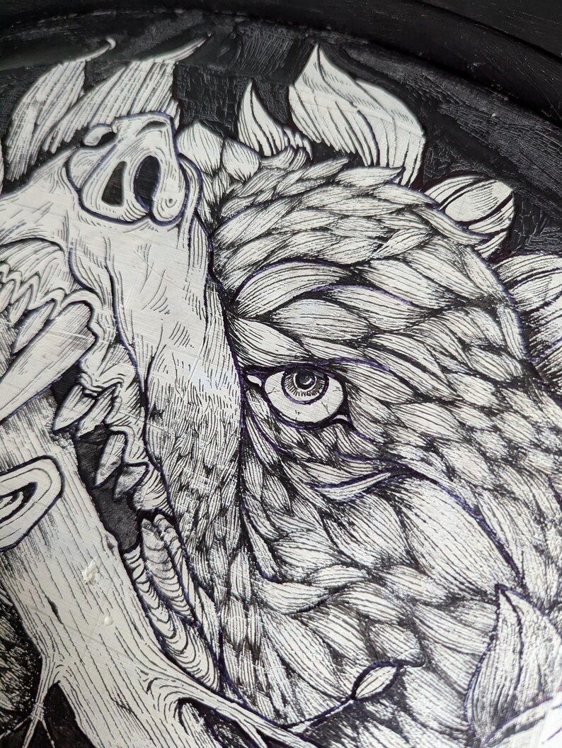 May include: A detailed black and white illustration of a wild boar's face, with intricate line work. The artwork includes a skull and foliage, creating a dramatic design. The image is a close-up, showing fine details.