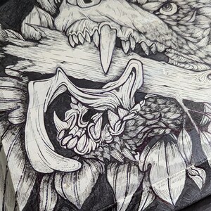 May include: Detailed black and white illustration of a wolf's head with exposed teeth biting a log. The artwork uses fine linework and is set against a dark background, creating a strong contrast. The image has a gothic or fantasy theme.