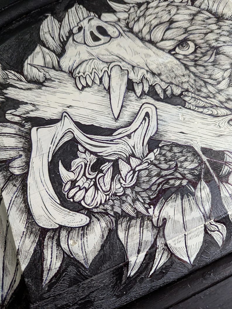 May include: Detailed black and white illustration of a wolf's head with exposed teeth biting a log. The artwork uses fine linework and is set against a dark background, creating a strong contrast. The image has a gothic or fantasy theme.