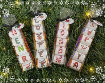 May include: Four cellophane-wrapped chocolate bars with Christmas-themed designs and text spelling out "HENNA" and "GIFT". Each bar features reindeer and holiday graphics. Tied with black ribbons and festive tags.