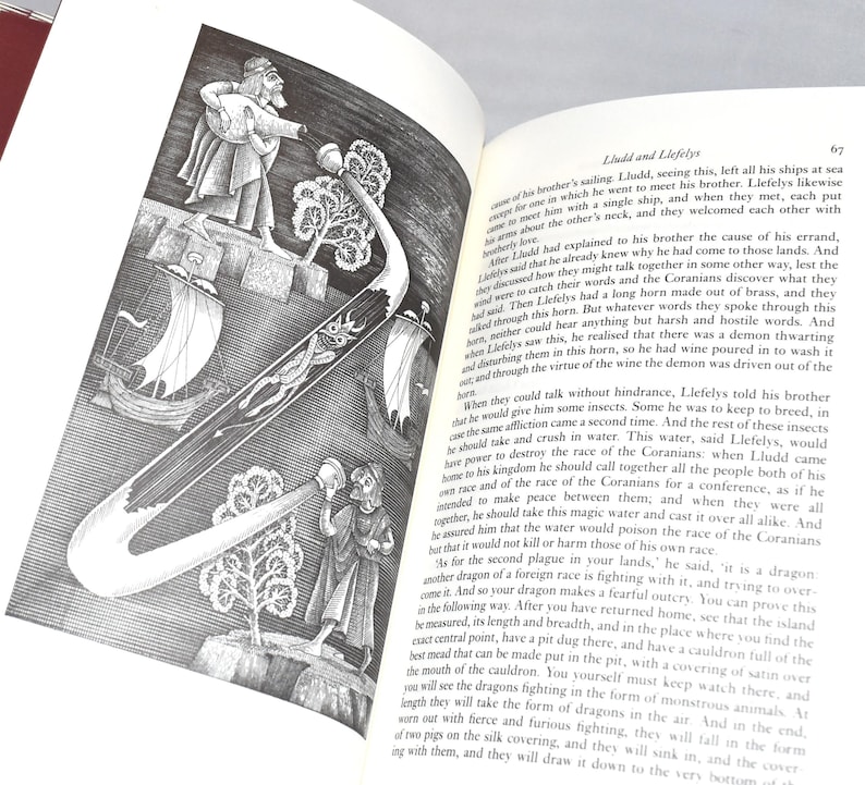 May include: An open book with a black and white illustration of a curved horn-like object with a detailed design, figures, and ships. The text on the page is in English.