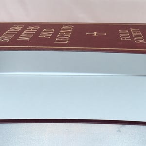 May include: A rectangular box with a maroon exterior and white interior. The top of the box features gold trim and the words "BRITISH MYTHS AND LEGENDS FOLIO SOCIETY" in gold lettering.