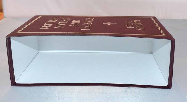 May include: A rectangular box with a maroon exterior and white interior. The top of the box features gold trim and the words "BRITISH MYTHS AND LEGENDS FOLIO SOCIETY" in gold lettering.