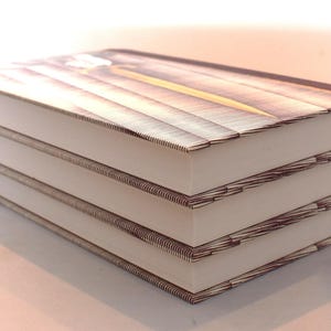 May include: A stack of three hardcover books with white pages and brown covers. The covers feature a wooden plank design with a yellow accent. The books are neatly stacked, suggesting a collection or set.