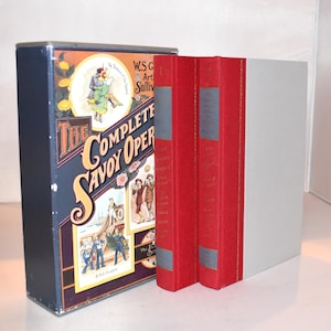 Peut inclure: Ensemble de livres intitulé "The Complete Savoy Opera" dans un coffret bleu marine avec des illustrations colorées. L'ensemble comprend des livres rouges avec des lettres dorées et un livre blanc.