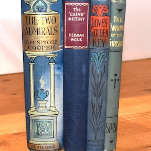 May include: A collection of four vintage hardcover books standing upright. The spines feature titles including The Two Admirals by J. Fenimore Cooper, The Caine Mutiny by Herman Wouk, Love's Golden Key, and The Winning of the Thread, with blue, red, and grey covers.