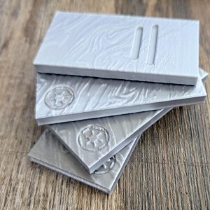 以下が含まれることがあります： 表面がテクスチャ加工されたグレーのプラスチックタイルが4枚。 上のタイルには、表面に平行な線が2本刻まれています。 他の3枚のタイルには、星形のエンボス加工が施されています。