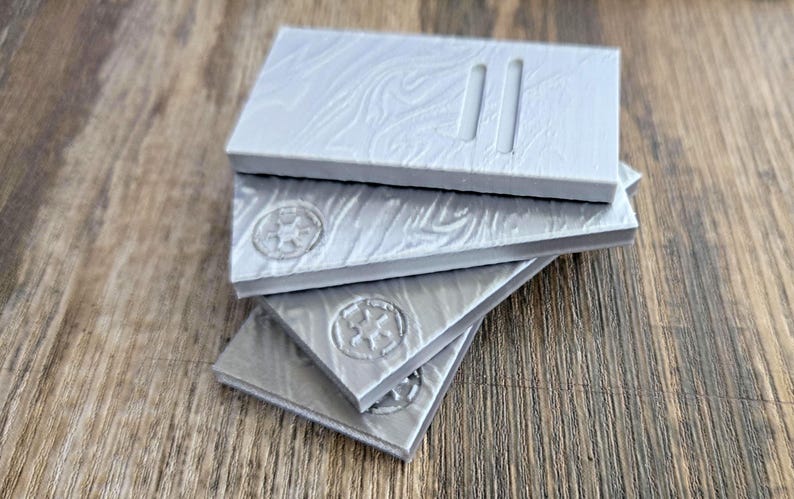 以下が含まれることがあります： 表面がテクスチャ加工されたグレーのプラスチックタイルが4枚。 上のタイルには、表面に平行な線が2本刻まれています。 他の3枚のタイルには、星形のエンボス加工が施されています。