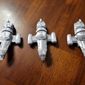 May include: Three gray 3D printed models of a spaceship, possibly from the show Firefly. The models are detailed and have a weathered look.
