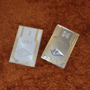 May include: Two white and silver plastic cards with gold trim. The cards have a raised design and the text "LEVEL 4" on them.