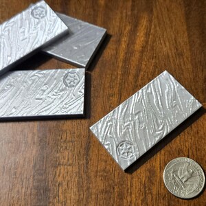 以下が含まれることがあります： 木製の表面に、質感のある表面と星形のシンボルが付いた銀色の金属棒が4本置かれています。棒は積み重ねられています。