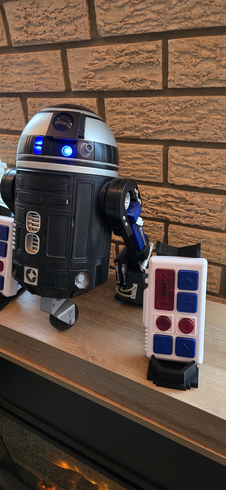 Peut inclure: Un jouet robot de style R2-D2 noir, argent et bleu avec une t&eacute;l&eacute;commande. Le jouet a un corps cylindrique, une t&ecirc;te en forme de d&ocirc;me et des bras articul&eacute;s. La t&eacute;l&eacute;commande est blanche avec des boutons bleus et rouges.