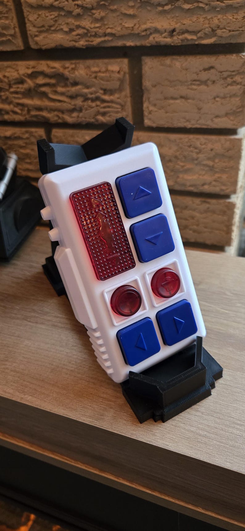 Peut inclure: Un appareil &eacute;lectronique blanc et noir avec des boutons bleus et rouges. L'appareil a une forme rectangulaire avec une s&eacute;rie de boutons et un panneau rouge textur&eacute;. Les boutons sont bleus avec des fl&egrave;ches blanches, et les panneaux rouges ont un motif circulaire.