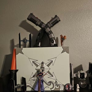 K&ouml;nnte beinhalten: Eine Pr&auml;sentation von Star Wars-Sammlerst&uuml;cken. Zwei gekreuzte Lichtschwerter sind &uuml;ber einer wei&szlig;en Box mit einem geometrischen Design positioniert. Weitere Artikel sind Miniatur-TIE-J&auml;ger, Figuren und ein rot-oranges Lichtschwert.