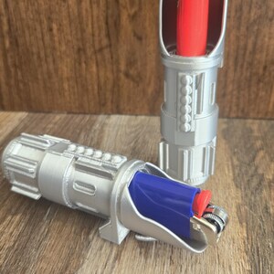 May include: Two silver lighters shaped like lightsabers. One lighter has a red lighter insert and the other has a blue lighter insert.