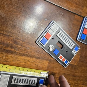 Op de afbeelding: Drie zwarte lichtschakelaars met een Star Trek-ge&iuml;nspireerd ontwerp. De afdekkingen hebben een grijs en zilveren bedieningspaneel met rode en blauwe knoppen.
