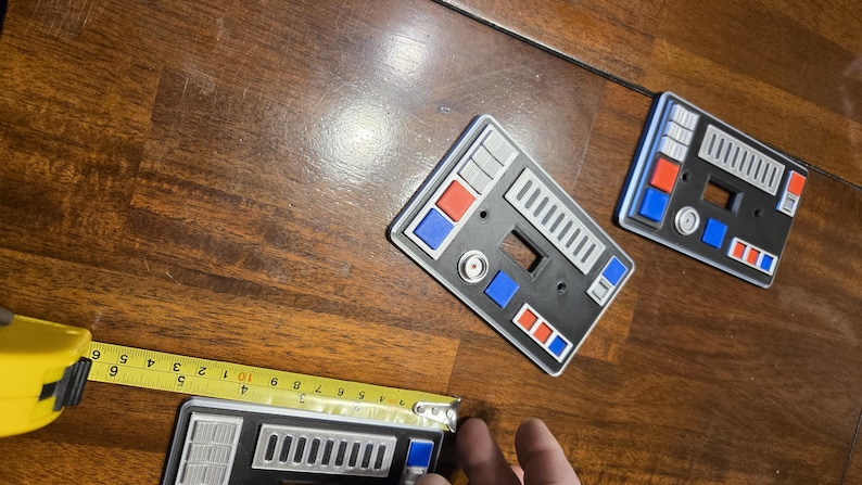 Op de afbeelding: Drie zwarte lichtschakelaars met een Star Trek-ge&iuml;nspireerd ontwerp. De afdekkingen hebben een grijs en zilveren bedieningspaneel met rode en blauwe knoppen.