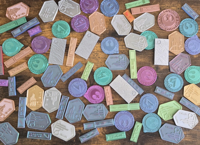 May include: A collection of colorful, round, and rectangular stickers with various designs. The stickers feature a variety of colors, including blue, green, purple, pink, and brown. The stickers are arranged on a wooden surface.