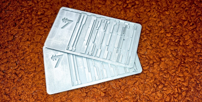 Peut inclure: Deux cartes rectangulaires gris clair avec une surface textur&eacute;e et un chiffre sept stylis&eacute;. Les cartes comportent une s&eacute;rie de lignes parall&egrave;les et perpendiculaires. Les cartes sont empil&eacute;es l'une sur l'autre.