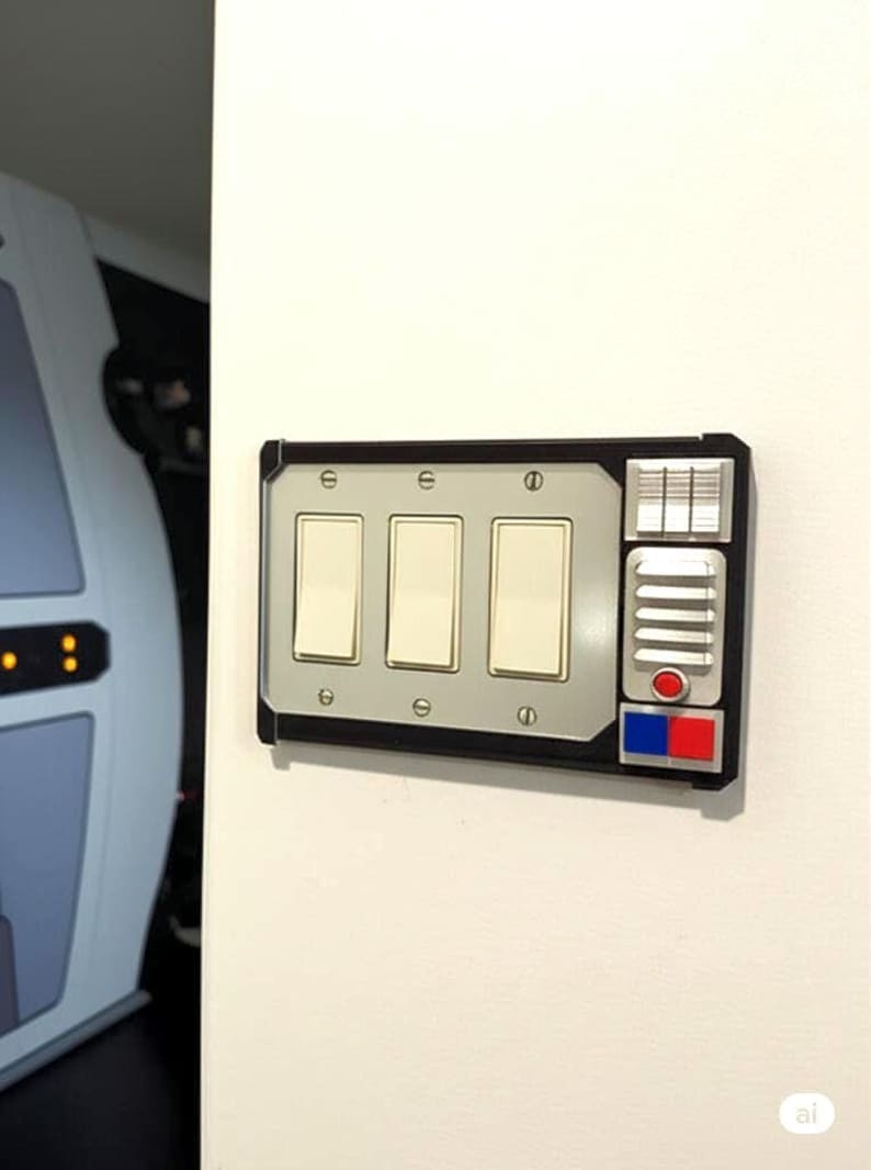 May include: A custom light switch plate with three light switches. The plate has a black frame with a silver center section. It features a control panel with red, blue, and silver accents, and is mounted on a white wall.