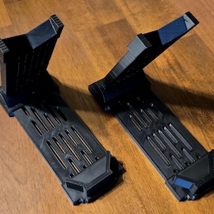 May include: Two black plastic display stands with a grid pattern on the base and a raised platform. The stands are designed to hold objects upright.
