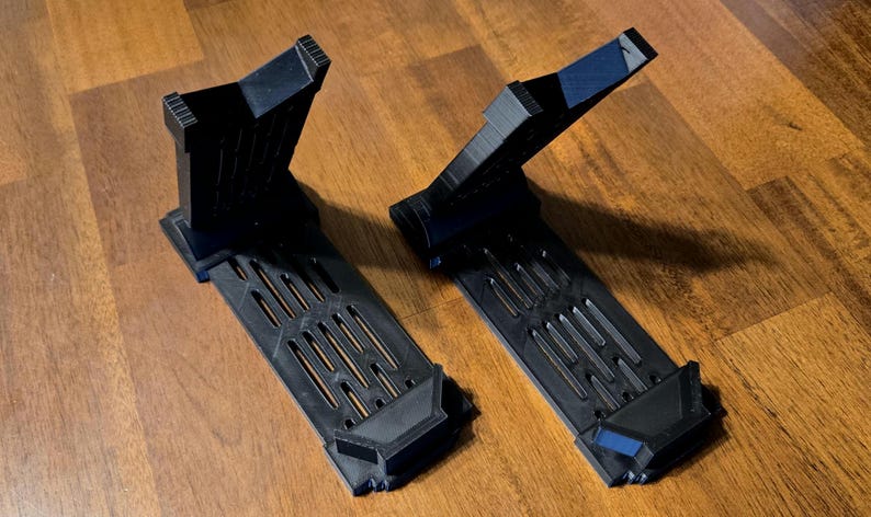 May include: Two black plastic display stands with a grid pattern on the base and a raised platform. The stands are designed to hold objects upright.