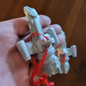 May include: A white 3D printed spaceship ornament with a red ribbon attached. The ornament is shaped like a spaceship with a pointed nose and wings.