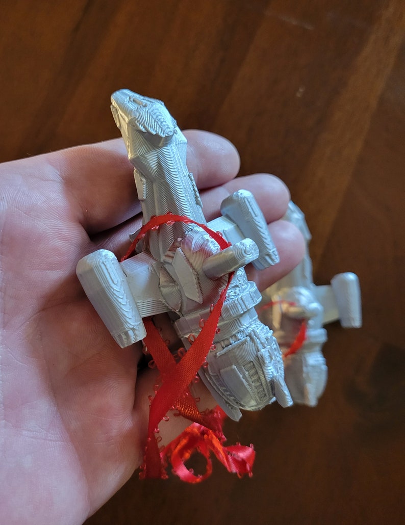 May include: A white 3D printed spaceship ornament with a red ribbon attached. The ornament is shaped like a spaceship with a pointed nose and wings.