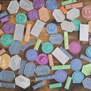 May include: A collection of colorful, round, and rectangular stickers with various designs. The stickers feature a variety of colors, including blue, green, purple, pink, and brown. The stickers are arranged on a wooden surface.