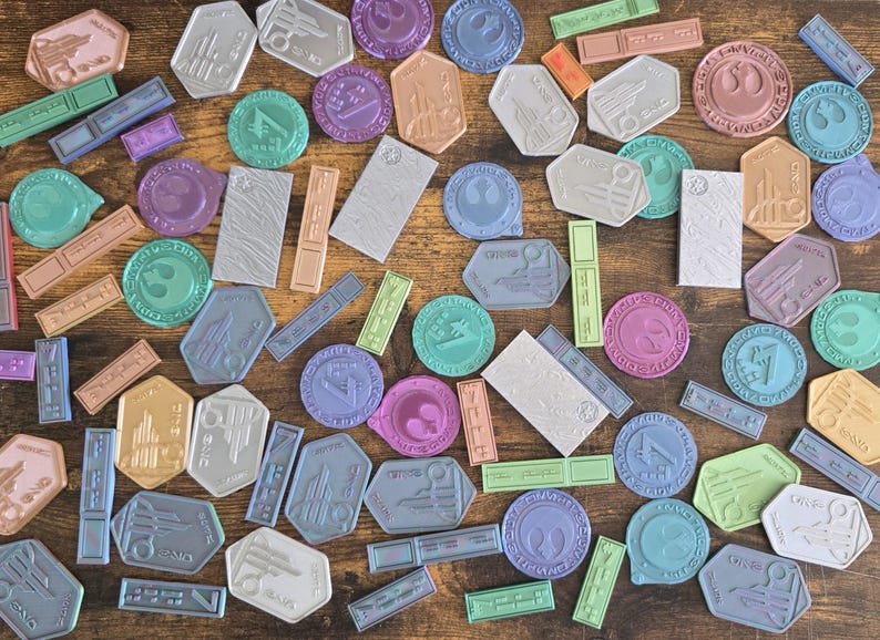May include: A collection of colorful, round, and rectangular stickers with various designs. The stickers feature a variety of colors, including blue, green, purple, pink, and brown. The stickers are arranged on a wooden surface.