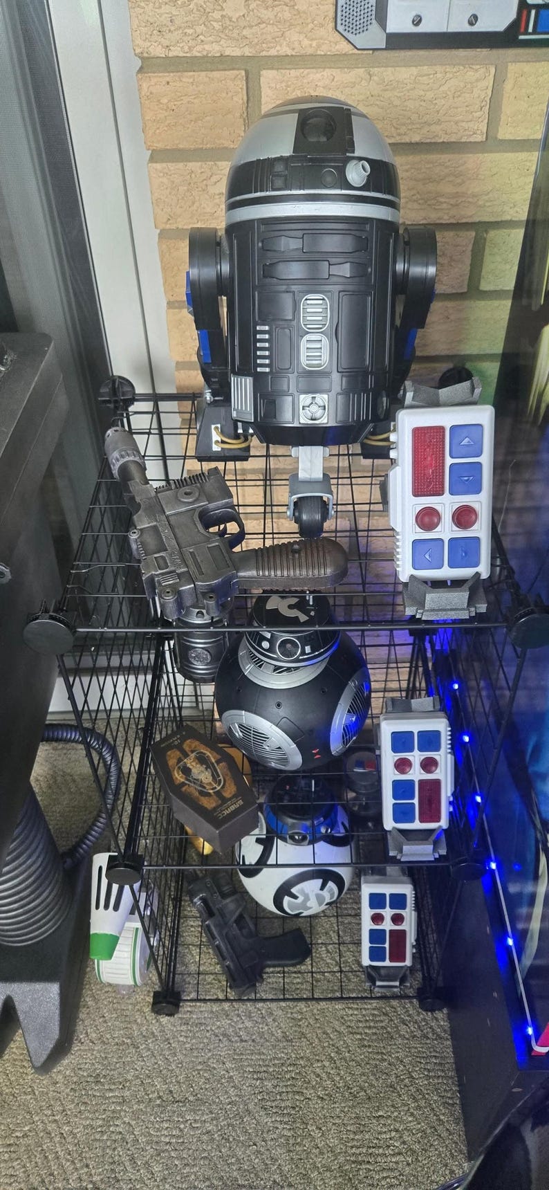 Peut inclure: Une collection de jouets et d'objets de collection sur le th&egrave;me de Star Wars, expos&eacute;e sur des &eacute;tag&egrave;res grillag&eacute;es. Comprend une grande figurine R2-D2 noire et argent&eacute;e, des dro&iuml;des BB-8, des blasters et des panneaux de contr&ocirc;le.