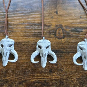 May include: Five identical white skull-shaped pendants with curved horns, each suspended from a thin brown leather cord. The pendants feature hollow eye sockets and a central nasal cavity, creating a distinct, symmetrical, and weathered appearance.