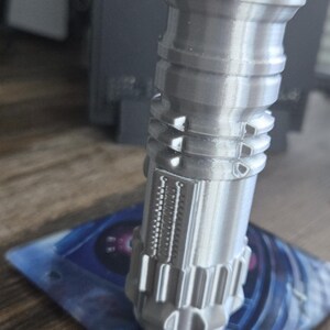 May include: A silver-colored lighter shaped like a lightsaber. The lighter has a red button on the top and a silver metal finish.