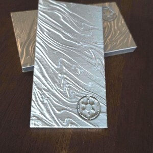 May include: Two silver metal business cards with a textured surface and a raised embossed logo of a star inside a circle.